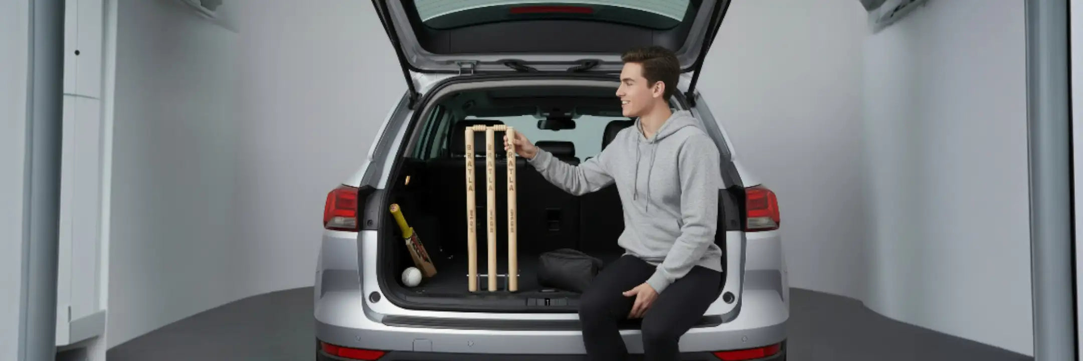 A set of wooden cricket stumps with a natural finish, positioned upright in the open trunk of a silver suv.