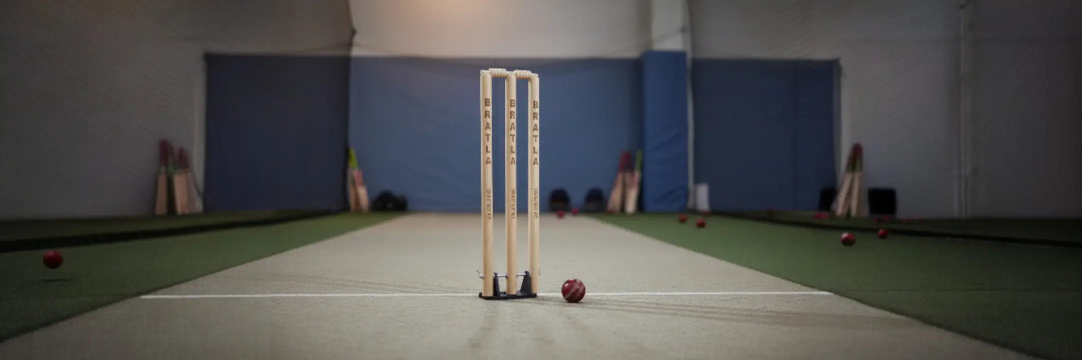 Three white cricket stumps with black bases and red stitching on the ball.